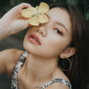 trendy asian woman covering eye with flower
